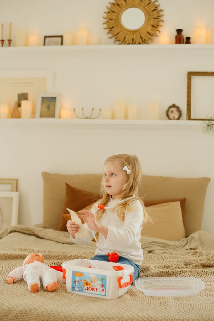 A cute child in a bedroom role-playing as a doctor with a toy kit and baby doll.
